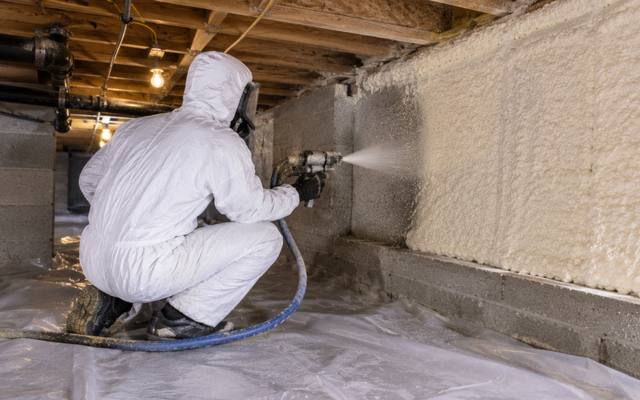 Installer sealing a crawl space wall over a taped ground sheet in full protective kit